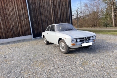 Frontansicht eines Alfa Romeo GTV 2000, Baujahr 1970er, in silberner Lackierung vor einer Holzscheune |  Alfa Romeo GTV 2000 – Frontansicht vor Scheune