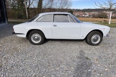 Rückansicht eines weißen Alfa Romeo GTV 1750 GT mit offener Landschaft im Hintergrund | Alfa Romeo GTV 1750 GT – Rückansicht und Umgebung