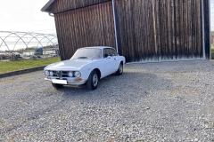 Frontalansicht eines weißen Alfa Romeo GTV 1750 GT vor rustikaler Scheune | Alfa Romeo GTV 1750 GT – Frontalansicht