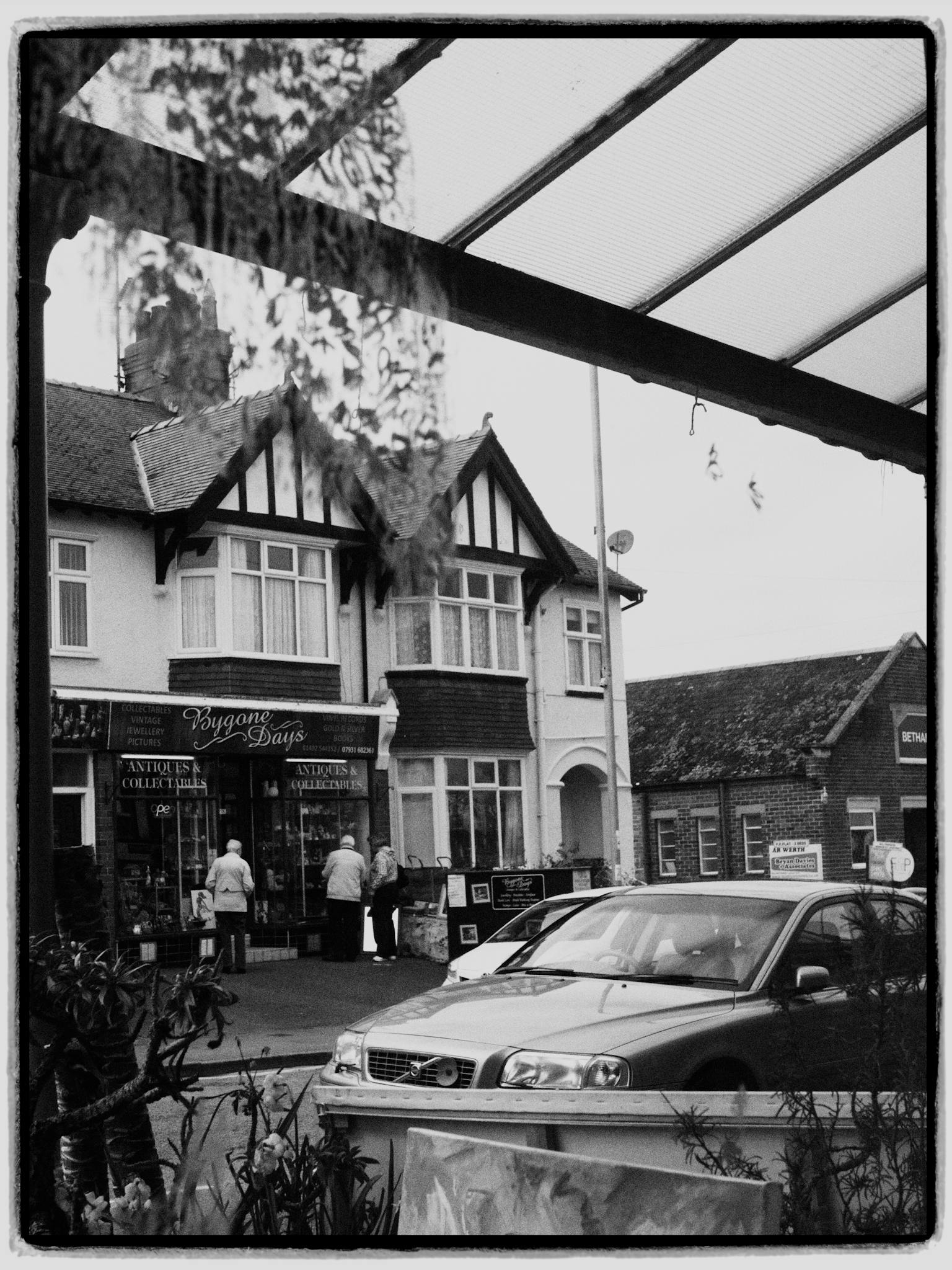 A black and white photo of a vintage street with classic architecture and a car parked in front.