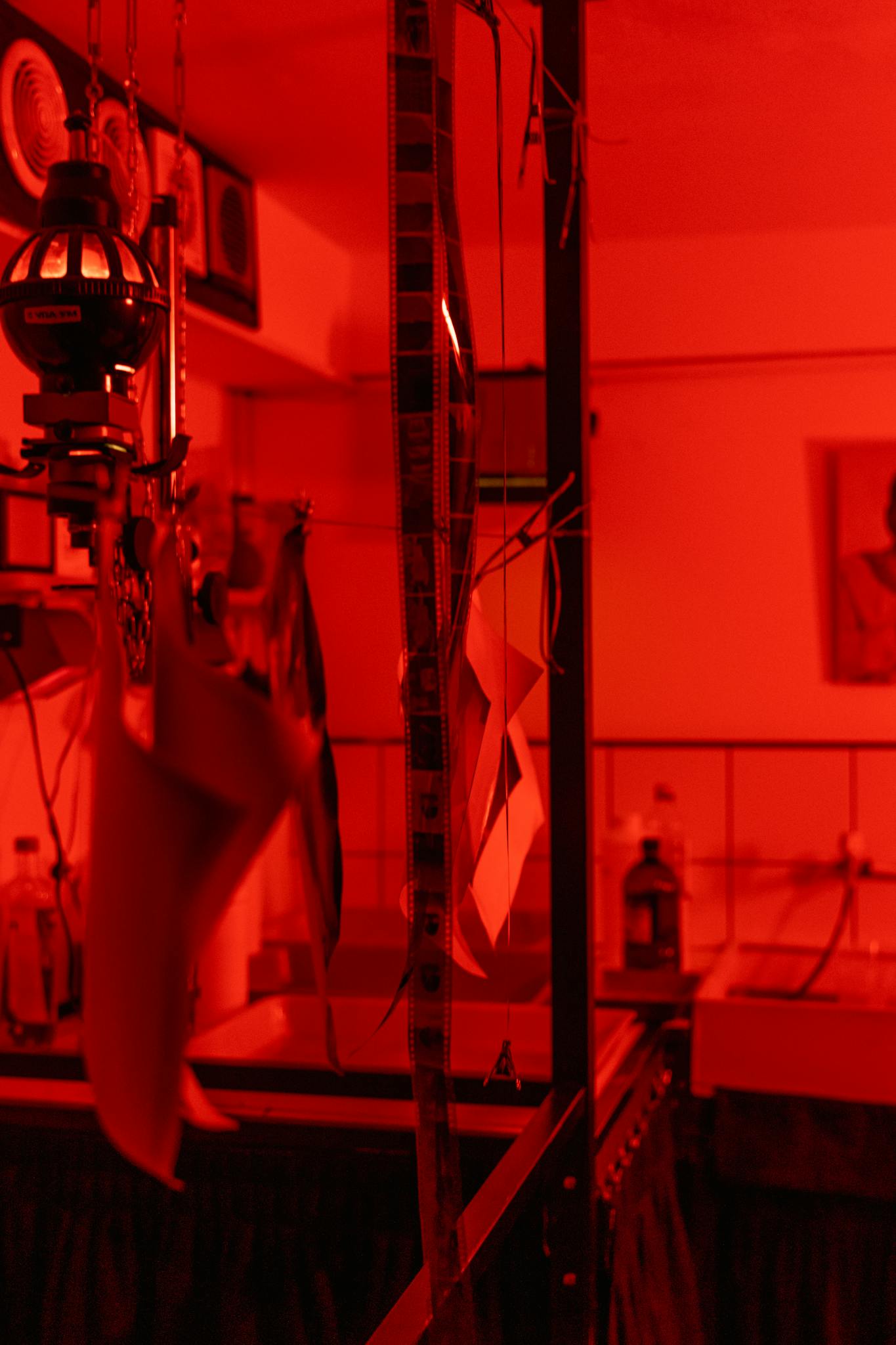 A detailed view of film developing process in a red-lit darkroom with negatives hanging.