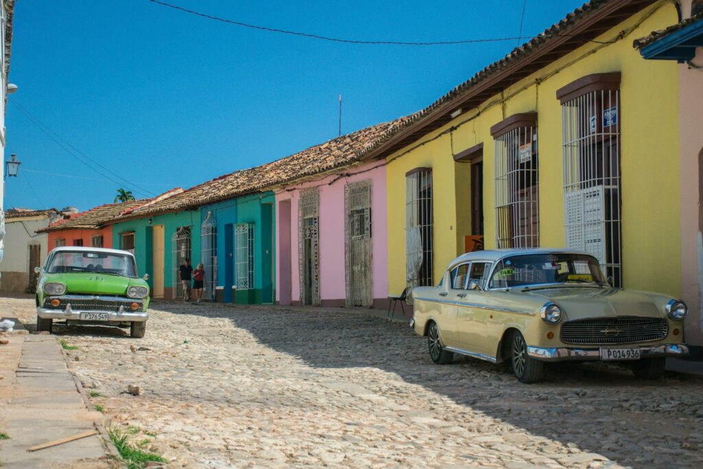 A vibrant street scene in Trinidad, Cuba with vintage cars parked along colorful colonial houses.