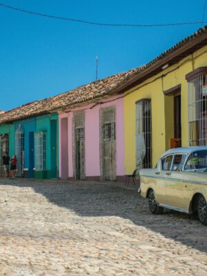 A vibrant street scene in Trinidad, Cuba with vintage cars parked along colorful colonial houses.