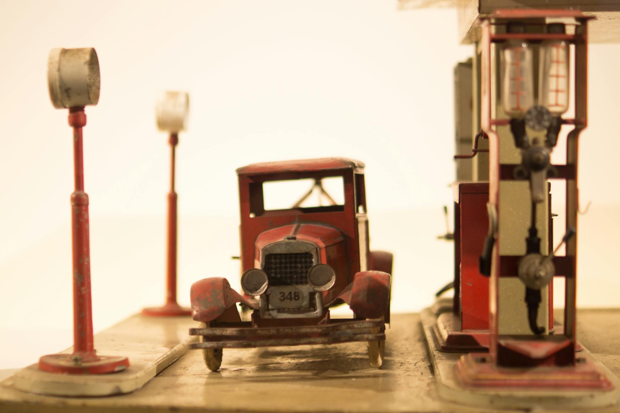 A vintage miniature car at an old-style gas station, showcasing retro automotive charm.