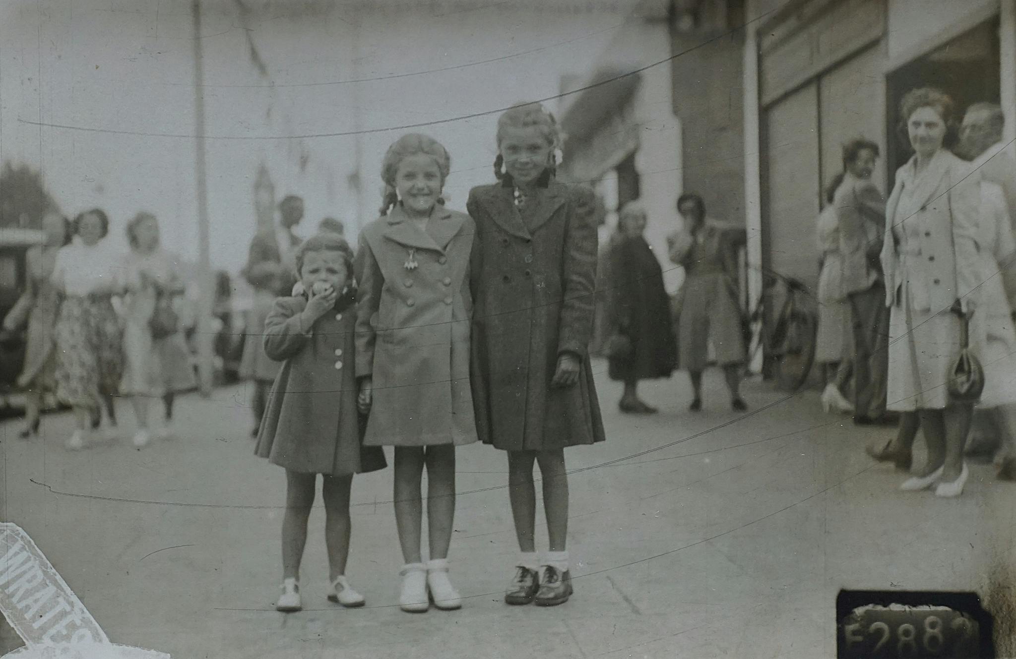 Charming vintage image shows three young girls smiling on a bustling street, evoking nostalgia and family memories.