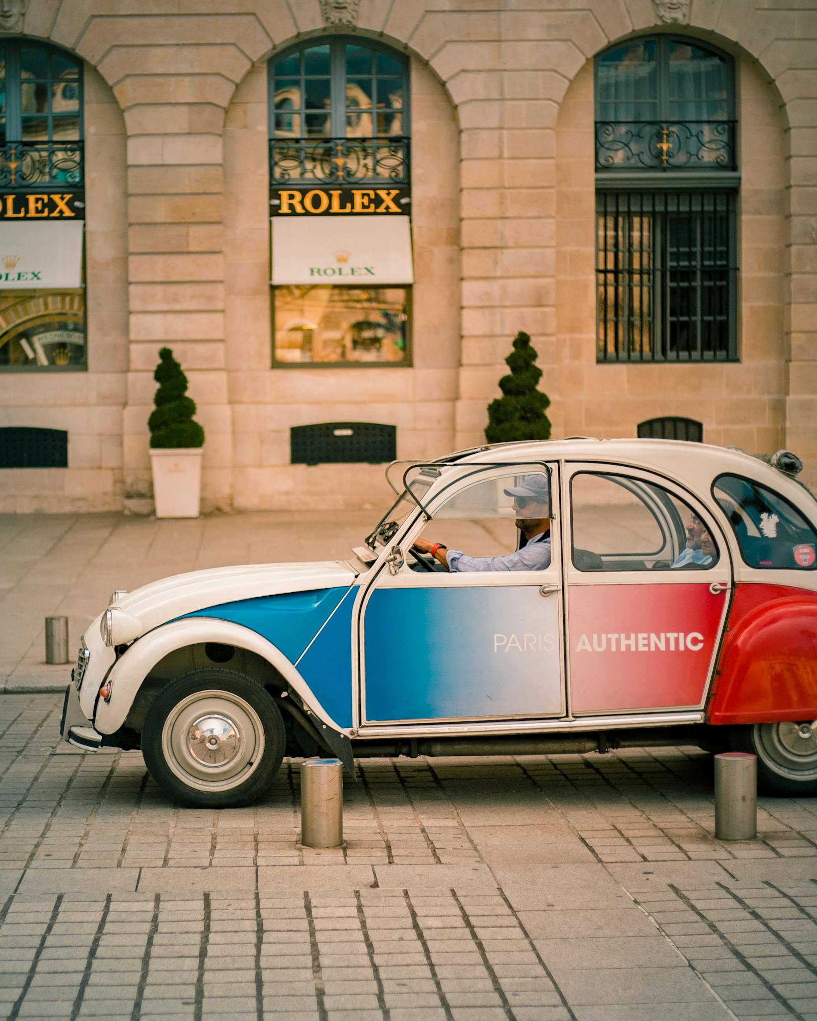 Classic French car parked in front of a Rolex store in Paris.