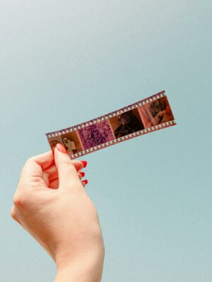 Close-up of a hand holding a film strip against a blue background, showcasing photography essentials.