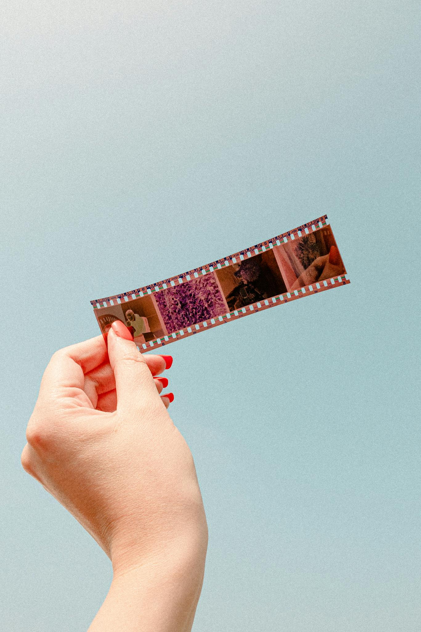 Close-up of a hand holding a film strip against a blue background, showcasing photography essentials.