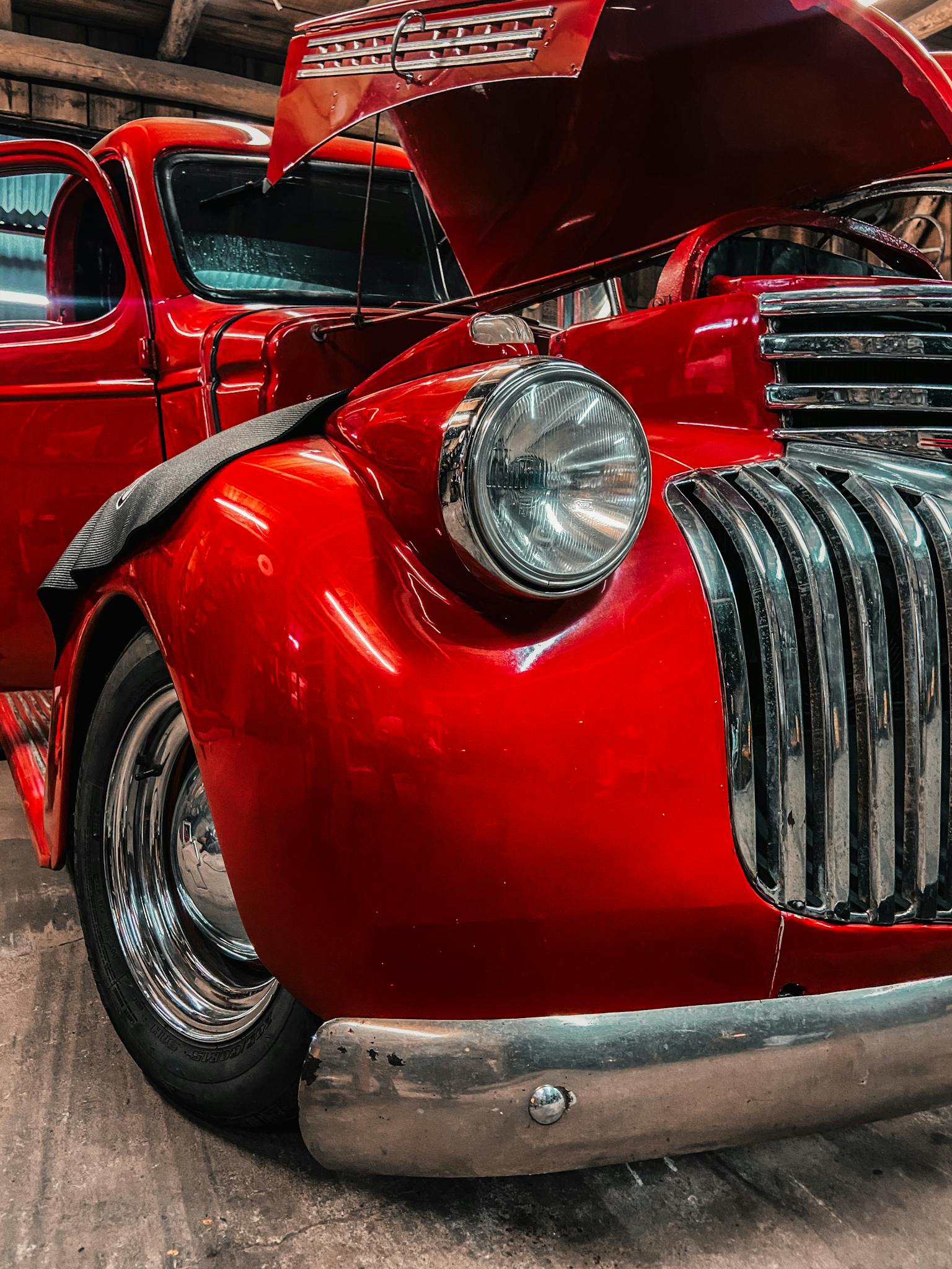 Close-up of a shiny red vintage car with open hood, showcasing classic design in a garage.